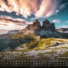 Kalendernummern und Wochentage sind in einer Reihe angeordnet. Der Text "Drei Zinnen, Dolomiten 10" ist prominent. Im Hintergrund sind beeindruckende Berggipfel bei Sonnenuntergang zu sehen.