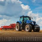 Kalender mit Daten und Wochentagen. Großer blauer Traktor zieht eine rote Landmaschine über ein Stoppelfeld.