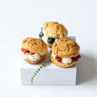 Drei gefüllte Windbeutel, garniert mit Johannisbeeren, Himbeeren und Blaubeeren auf einer weißen Box.