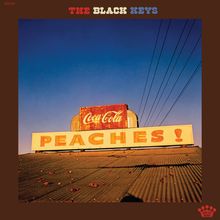"PEACHES!" und "Coca-Cola" auf einem nostalgischen Schild vor blauem Himmel. Oben steht "The Black Keys".