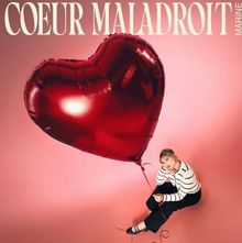 Text: "COEUR MALADROIT", "MARINE".  
Eine Frau sitzt auf rosa Boden, hält einen großen, roten Herzballon.