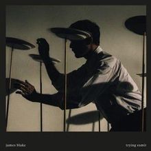 Text: "james blake", "trying 2 sml". Ein Mann balanciert mehrere Teller auf Stangen in gedämpftem Licht.