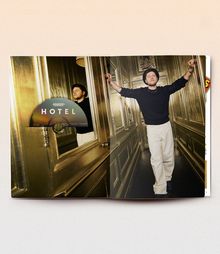 Text: "JOHANNES OERDING HOTEL". 

Ein Mann steht lässig in einem goldenen Gang und stützt sich an den Wänden ab.