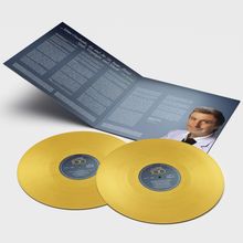 Zwei goldene Schallplatten liegen vor einem geöffneten blauen Cover mit viel Text und einem Bild eines Mannes in hellblauem Anzug.