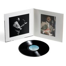 Eine Schallplattenhülle zeigt zwei Fotos eines Mannes mit Gitarre. Eine schwarze Vinyl-Schallplatte liegt davor.