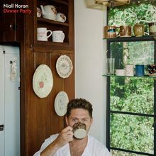 Niall Horan, Dinner Party. Ein Mann sitzt in einer Küche, trinkt aus einer Tasse. Fenster und Geschirr im Hintergrund.