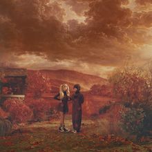 Zwei Personen stehen in herbstlicher Landschaft mit dramatischem Himmel, umgeben von Laub und Bäumen.