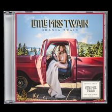 "LITTLE MISS TWAIN, SHANIA TWAIN. Eine Frau sitzt in einem roten Pickup. Landschaft mit Bäumen im Hintergrund."