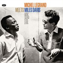 "Michel Legrand Meets Miles Davis" in großen Buchstaben. Zwei Männer stehen und unterhalten sich lebhaft in einem Studio.