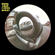 "THIN LIZZY" oben links, Fotografie eines Oldtimers in Fischaugenperspektive, umgeben von Wohnhäusern auf einer Straße.