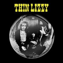 Text "THIN LIZZY" in gelb. Schwarz-Weiß-Foto von drei Personen, die eine entspannte Pose einnehmen.