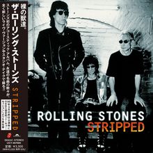 "ROLLING STONES STRIPPED." Drei Personen in schwarz-weißer Kleidung, zwei sitzen, eine steht vor einer Backsteinmauer.
