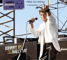Text: "JOHNNY ARCHIVES LIVE", "FÊTE DE L'HUMA", "15 SEPTEMBRE 1985", "JOHNNY 85 HALLYDAY". Mann in weißem Sakko mit Mikrofon auf Bühne.