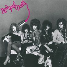 „New York Dolls“ in pinker Schrift. Schwarz-weiß Foto von fünf Personen auf einem Sofa, auffällig gestylt.