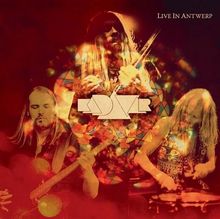 „Live in Antwerp“ und „Kadavar“ in stilisiertem Text, drei Musiker mit Instrumenten in psychedelischen Farben.