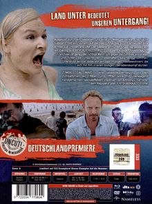 „Land unter bedeutet unseren Untergang!“ Eine blonde Frau schreit, während unten ein Mann und andere Menschen am Strand stehen.