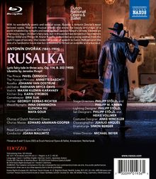 "RUSALKA" in großen Buchstaben. Darunter Besetzung und Team der Oper. Eine vermummte Figur mit Gewehr im dunklen Raum.