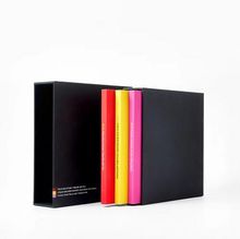 Vier bunte, schmale Bücher (schwarz, orange, gelb, pink) mit unlesbarem Text auf den Buchrücken.