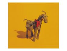 Keine Texte sichtbar. Eine kunstvolle Strohziege mit roter Schleife vor gelbem Hintergrund.