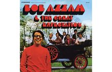 Text: "BOB AZZAM & THE GREAT EXPECTATION". Ein Mann im roten Pullover lächelt, im Hintergrund Personen in einem Auto.