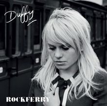 Text: Oben links „Duffy“, unten links „ROCKFERRY“. Schwarz-weißes Porträt einer nachdenklichen Frau vor einem Zug.