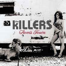 "The Killers Sam's Town" in Schwarz und Rot auf einer Mauer. Frau in Bikini und Schärpe, Widder liegt auf steinigem Boden.
