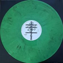 Kreisschrift: "prophecy". Grüne Schallplatte mit zentralem schwarz-weißem Symbol auf weißem Etikett.