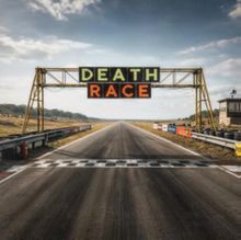 Text "DEATH RACE" auf Banner über Rennstrecke. Lange, leere Straße mit Ziellinie, umgeben von Reifenstapeln.