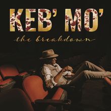 Text: "KEB' MO'", "the breakdown". Ein Mann mit Hut sitzt lächelnd entspannt in einem Theatersaal auf roten Sitzen.