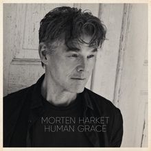"Morten Harket Human Grace." Schwarz-weiß Portrait eines nachdenklich schauenden Mannes vor einer alten Tür.