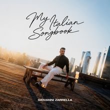 "My Italian Songbook" und "Giovanni Zarrella"; Mann sitzt auf Bank mit Stadt im Hintergrund bei Sonnenuntergang.