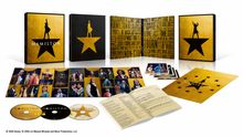 "HAMILTON" steht auf einem goldenen Hintergrund mit schwarzem Stern und Figur. Fotos von Bühnenszenen und CDs sind sichtbar.