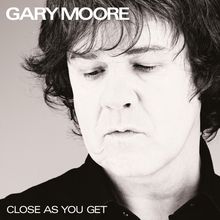 Text: "GARY MOORE" oben links, "CLOSE AS YOU GET" unten links. Schwarz-weiß Foto einer Person mit geschlossenen Augen.