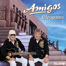 Titel: Amigos - Cleopatra. Zwei Männer sitzen vor einem Gebäude, einer hält eine Gitarre.