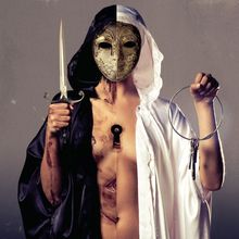 Eine Person trägt eine geteilte Maske, hält ein Schwert und Schlüssel, und trägt schwarze und weiße Roben.