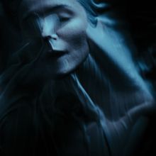 Eine abstrakte, dunkelblaue Darstellung eines Gesichts, das unter verzerrtem Stoff verborgen wirkt.