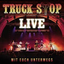 "TRUCK STOP LIVE", "MIT EUCH UNTERWEGS" steht in großen Buchstaben. Eine Band spielt beleuchtet auf einer Bühne.