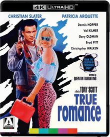 "TRUE ROMANCE" in großer blauer Schrift, mit Christian Slater und Patricia Arquette. Mann mit Waffe, Frau in Sonnenbrille.