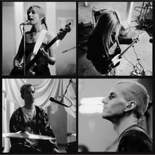 Keine sichtbaren Texte. Vier Personen musizieren: eine Sängerin mit Bass, ein Gitarrist, ein Schlagzeuger, ein Porträt. Schwarz-Weiß.