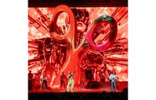 Die Bühne zeigt ein übergroßes rot-goldenes Scheren-Symbol vor einer futuristischen, roten Illustration. Musikgruppe spielt.