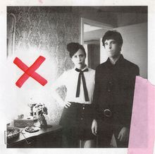 Rotes X auf einem Schwarz-Weiß-Foto. Zwei Personen stehen in einem Raum mit gemusterten Tapeten.