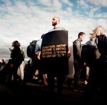 Ein Mann in einer Gruppe trägt ein Schild: "I know you're hurting, everyone is hurting, everyone is trying, you have got to try."