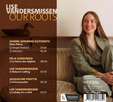 "LISE VANDERSMISSEN OUR ROOTS" oben links, eine lächelnde Frau sitzt rechts, ein Holzenten-Modell links.