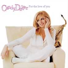„Candy Dulfer, For the love of you“. Eine Frau in Weiß sitzt auf einem Sessel, ein Saxophon lehnt neben ihr.