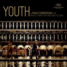 "YOUTH" und "A Paolo Sorrentino Film" oben links, zwei Personen spazieren vor beleuchtetem Gebäude, elegante Architektur.