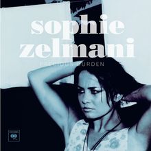 "sophie zelmani, PRECIOUS BURDEN" in Weiß. Eine Frau mit zurückgekämmtem Haar hält den Arm über dem Kopf.
