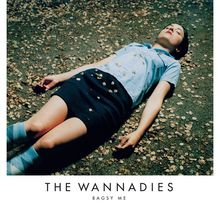THE WANNADIES - BAGSY ME. Eine Person in Sommerkleidung liegt entspannt auf dem Boden, umgeben von Blättern.