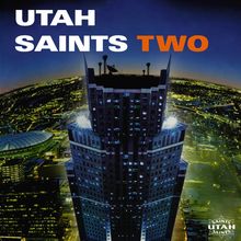 "UTAH SAINTS TWO" in weiß und orange auf dunklem Hintergrund, darunter eine nächtliche Stadtansicht mit beleuchtetem Hochhaus.
