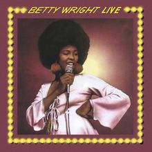 "BETTY WRIGHT LIVE" steht oben in gelber Schrift. Eine Frau singt mit Mikrofon, in einem lila Rahmen mit gelben Lichtern.