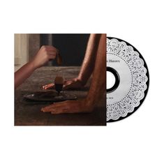 Ein CD-Design mit einem Spitzenmuster und der Titel "Burning Heights". Daneben eine Szene mit Händen über einem Tisch.